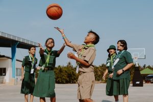 Group of children in school uniforms playing basketball outdoors, enjoying a sunny day.